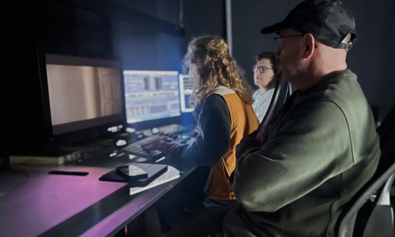 Professionals collaborating in a darkened post-production suite, focusing on color grading and visual effects work. The team is working with advanced editing software on a multi-monitor setup, immersed in the creative process of refining film footage for high-end projects in the film and television industry.